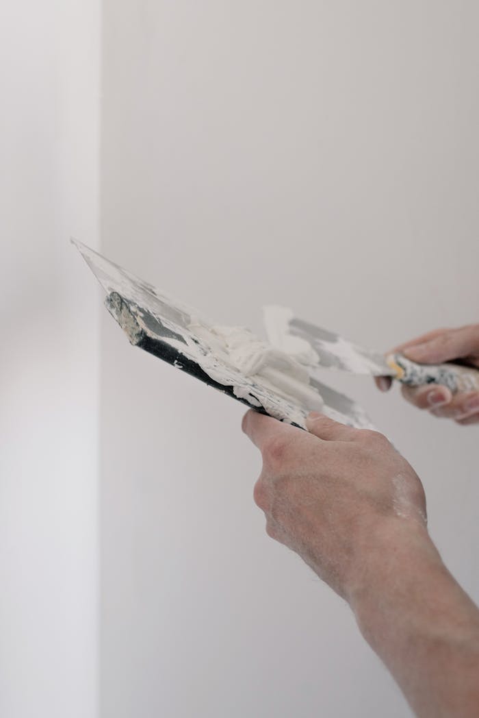 Crop unrecognizable male worker holding metal putty knives while working in room at home