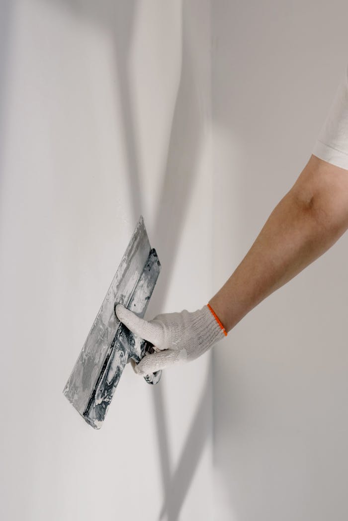 Crop anonymous male worker in gloves holding putty knife while working at home