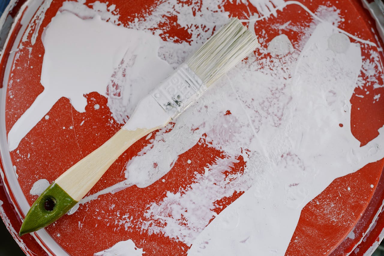 From above of brush with white paint on dirty plastic surface during repair